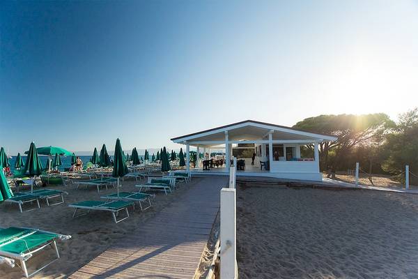Strandansicht des Club Hotel Marina Beach mit Liegen, Sonnenschirmen und einem Gebäude