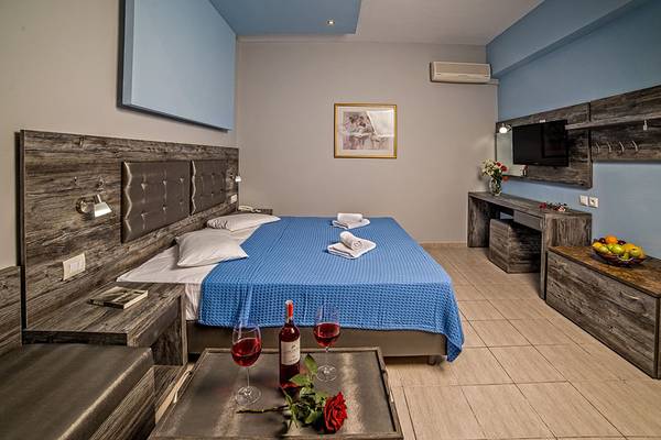 Zimmer im Blue Aegean Hotel & Suites mit Doppelbett, Weinflaschen und Rosen.