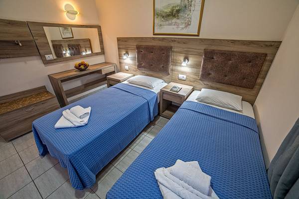 Zwei Betten im Hotelzimmer mit blauen Bettdecken und weißen Kissen, neben einem Tisch mit Obstschale.