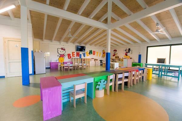 Ein buntes Kinderspielzimmer im Club Hotel Marina Beach mit langen Tischen, Stühlen und einem Fernseher an der Wand.