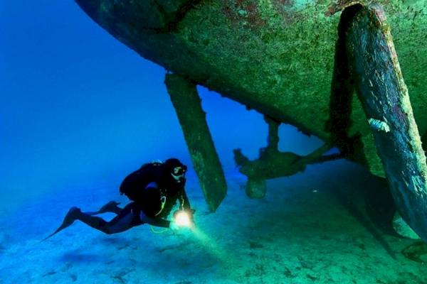 Taucher mit Taucherlampe unter einem großen Schiffspropeller im Wasser