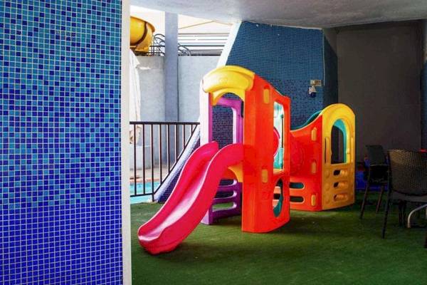 Spielplatz im AX Odycy Hotel mit bunten Spielgeräten, Rutsche und Tisch mit Stühlen.