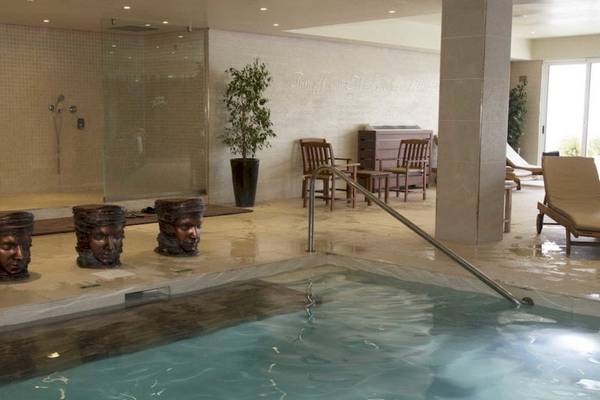 Innenbereich des Schwimmbads im AX Odycy Hotel mit Wasser, Marmorboden und dekorativen Elementen.