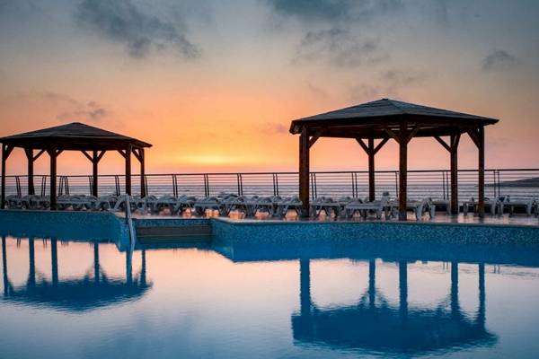 Sonnenuntergang am AX Odycy Hotel Pool mit zwei Holzpavillons und Sonnenliegen