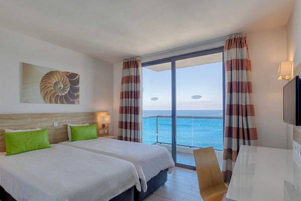 Zimmer im AX Odycy Hotel mit Blick auf das Meer und zwei Betten, einer davon hat grüne Kissen.