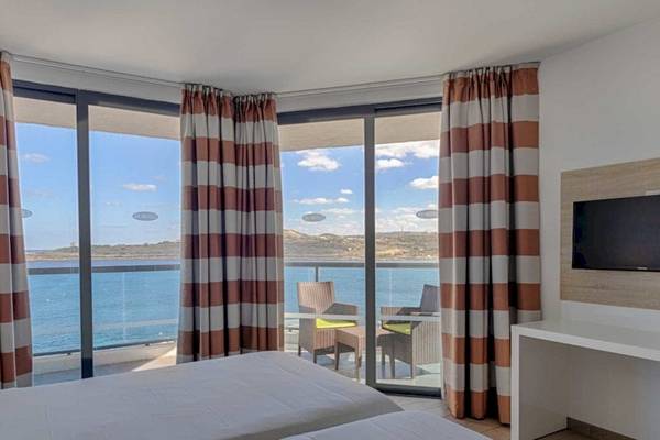 Zimmer im AX Odycy Hotel mit Blick auf das Meer, zwei Betten, Sessel und Tisch auf dem Balkon.