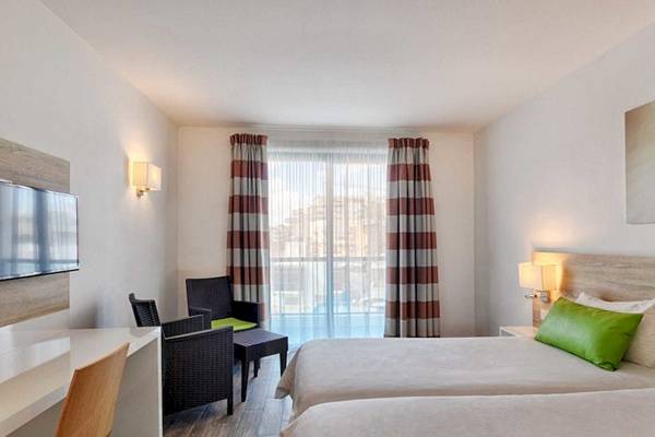 Innenansicht eines Doppelzimmers im AX Odycy Hotel mit zwei Betten, Schreibtisch, Stühlen und Fernseher.