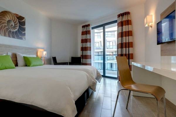 Doppelzimmer im AX Odycy Hotel mit zwei Betten, grünen Kissen, Schreibtisch und Balkonzugang.