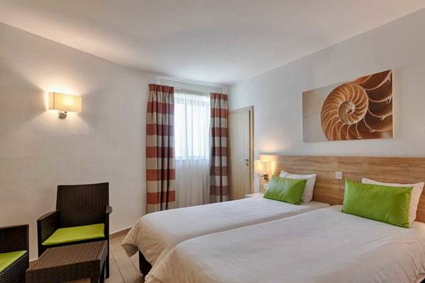 Doppelzimmer im AX Odycy Hotel mit zwei Betten, weißen Laken, grünen Kissen und weißen Wänden.