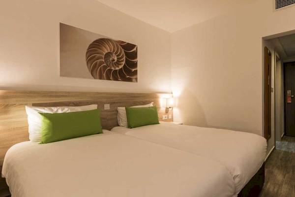 Doppelbettzimmer im AX Odycy Hotel mit zwei weißen Betten, grünen Kissen und einer modernen Einrichtung.