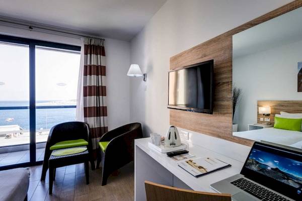 AX Odycy Hotelzimmer mit Meerblick, Laptop, Schreibtisch, Sessel und Fernseher.