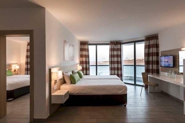 AX Odycy Hotel Zimmer mit Meerblick, zwei Betten, Fernseher, Schreibtisch und Panoramafenstern.