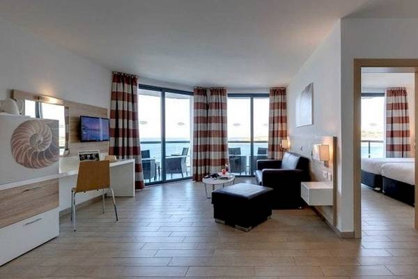 Innenansicht des AX Odycy Hotels, Wohnbereich mit Sofa, Fernseher und Ausblick auf das Meer.