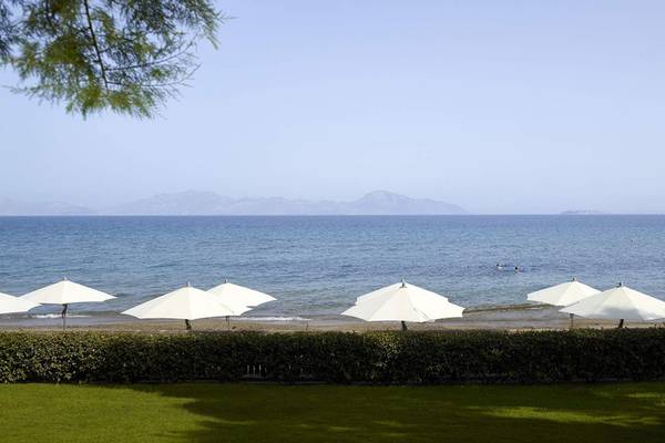 Strandansicht des Neptune Luxury Resorts mit weißen Sonnenschirmen und blauem Meer