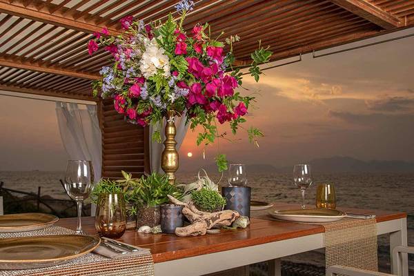 Tisch im Neptune Luxury Resort mit Meerblick und Blumenarrangement bei Sonnenuntergang.