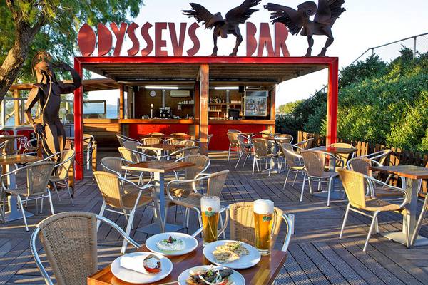Terrasse des Odysseus Bar im Neptune Luxury Resort mit Tischen, Stühlen und Getränken.