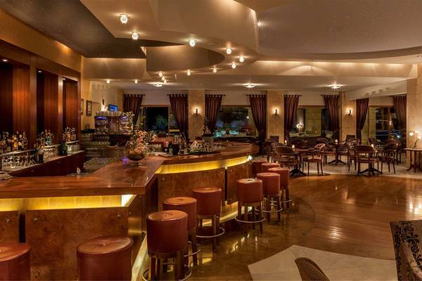 Innenansicht der Bar im Neptune Luxury Resort mit Holzboden, roten Stühlen und einer Theke voller Flaschen.