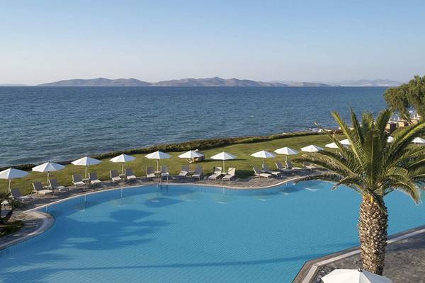 Außenpool des Neptune Luxury Resort mit Blick auf das Meer, umgeben von Sonnenliegen und weißen Sonnenschirmen.