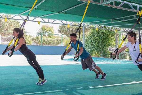 Drei Personen, die ein Training mit Fitnessgurten in einem überdachten Bereich im Freien durchführen.