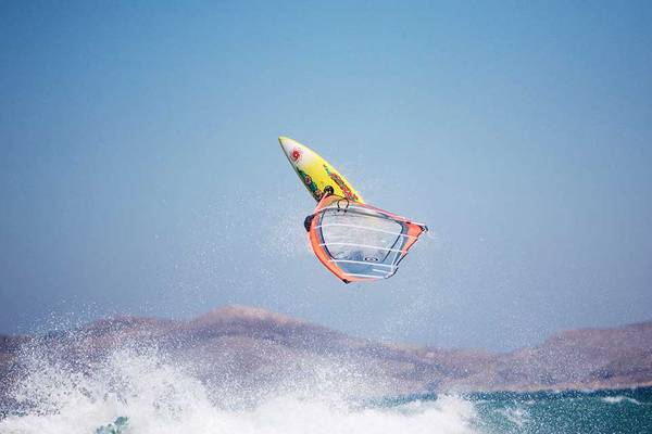 Windsurfer im Meer auf Wellen mit farbigem Segel und blauem Himmel im Hintergrund.
