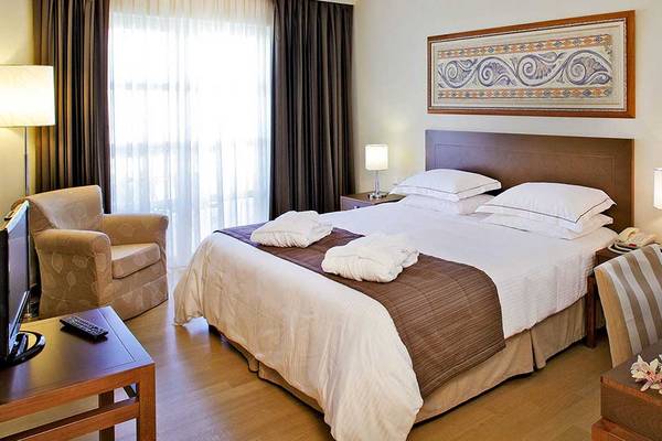 Hotelzimmer im Neptune Luxury Resort mit Bett, Kissen, Fernseher, Lampe und Schreibtisch