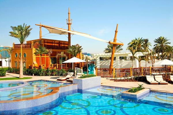 Außenbereich des St. Regis Abu Dhabi mit einem großen Schwimmbad und einem gelben Gebäude, das wie ein Schiff aussieht.