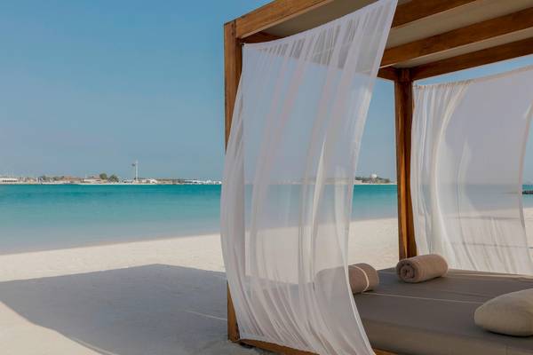 Bett auf dem Strand vor dem St. Regis Abu Dhabi Hotel mit weißen Vorhängen und Blick auf das Meer.