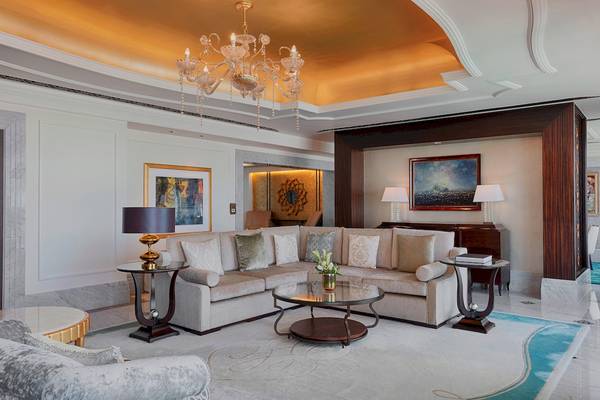 Wohnzimmer im St. Regis Abu Dhabi mit goldener Decke, Kristallkronleuchter, beige Sofa und blauem Teppich