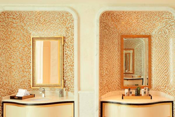 Badezimmer im St. Regis Abu Dhabi mit goldenen Fliesen, zwei Waschbecken und Spiegeln.