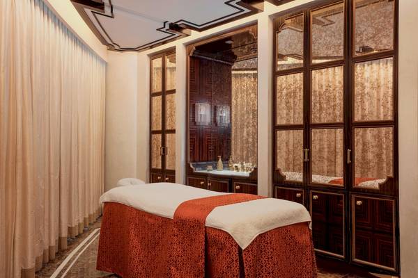 Spa-Behandlungsraum im St. Regis Abu Dhabi mit orangefarbener Liege und cremefarbenen Vorhängen.