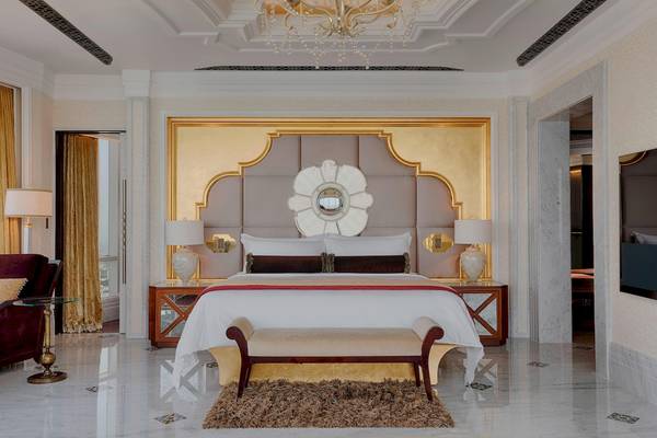 Schlafzimmer im St. Regis Abu Dhabi Hotel mit goldenem Kopfteil, großem Bett, zwei Lampen und Kristallkronleuchter.