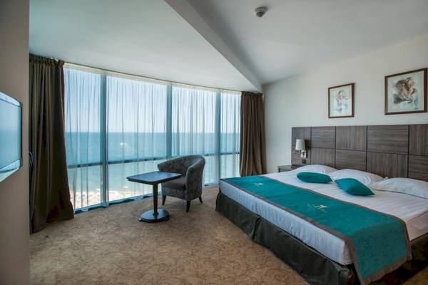 Zimmer im Marina Grand Beach Hotel mit Blick auf das Meer von einem großen Bett aus.