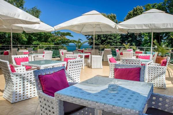 Außenterrasse des Marina Grand Beach Hotels mit Tischen und Stühlen unter weißen Sonnenschirmen.