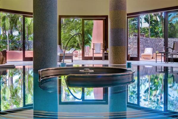 Innenansicht des Schwimmbeckens im Tivoli La Caleta Tenerife Resort mit Loungebereich und Glastüren.