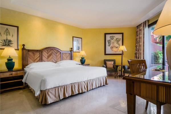 Doppelbett im Hotelzimmer von Tivoli La Caleta Tenerife Resort mit gelben Wänden und Holzmöbeln