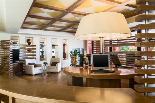 Empfangsbereich im Tivoli La Caleta Tenerife Resort mit moderner Einrichtung, Holzmöbeln und einer großen Lampe.