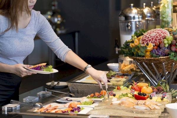 Frau bedient ein Buffet im Beyond Resort Krabi mit verschiedenen Speisen und Früchten.