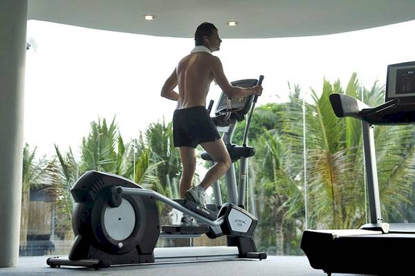 Ein Mann trainiert auf einem elliptischen Trainer im Fitnessstudio mit Blick auf Palmenbäume.