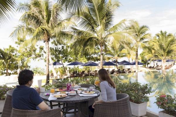 Paar genießt Frühstück im Freien im Beyond Resort Krabi mit Blick auf den Pool und Palmen