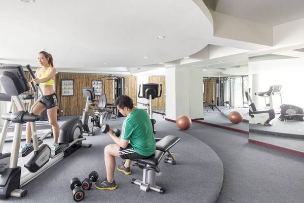 Fitnessstudio im Beyond Resort Krabi mit einer Frau auf dem Laufband und einem Mann, der Gewichte hebt.