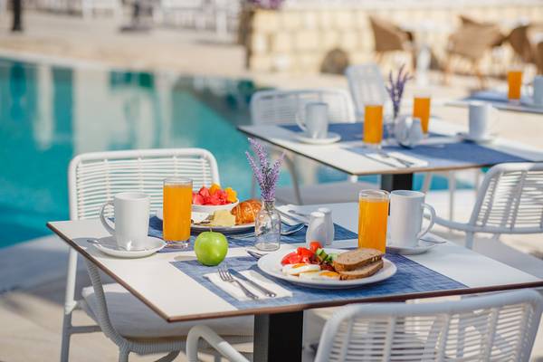 Frühstückstisch am Pool im Louis St. Elias Resort & Waterpark mit Früchten, Brot und Orangensaft.