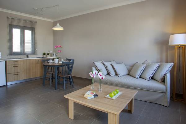 Wohnzimmer des Louis St. Elias Resorts mit Sofa, Tisch, Lampe und Küche im Hintergrund.