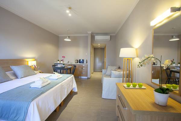 Ein modernes Hotelzimmer im Louis St. Elias Resort & Waterpark mit Bett, Tisch, Stühlen und Küchenbereich.