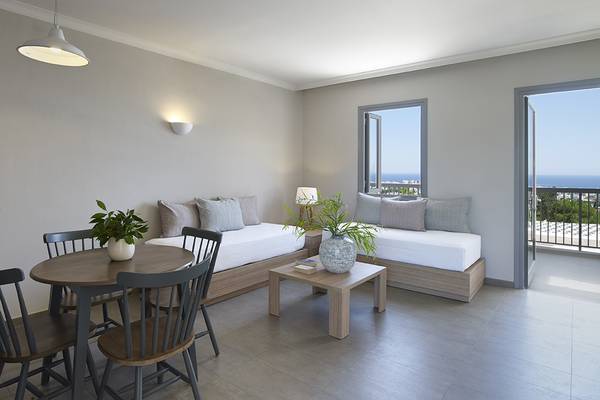 Innenansicht einer Suite im Louis St. Elias Resort & Waterpark mit zwei Betten, Tisch, Stühlen und Ausblick auf das Meer.