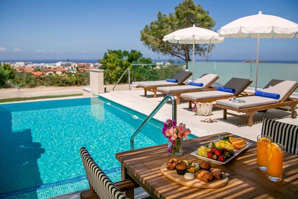 Pool-Loungebereich im Louis St. Elias Resort mit Sonnenliegen und Frühstückstablett.