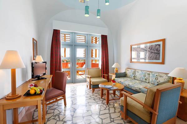 Innenansicht eines modernen Hotelzimmers mit Möbeln, Fernseher, Schreibtisch und Früchten.