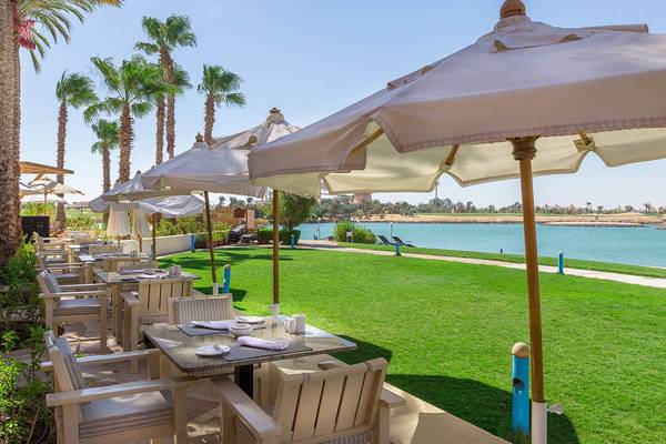 Außenterrasse des Steigenberger Golf Resort El Gouna mit Tischen und Stühlen unter Sonnenschirmen vor einem See.