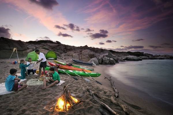 Familien-Campingplatz am Strand mit aufgestellten Kajaks, Zelten und einem brennenden Lagerfeuer