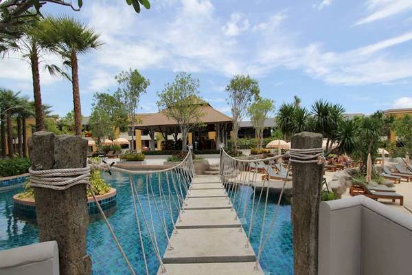 Brücke über den Pool im Rawai Palm Beach Resort mit Palmen und Lounge-Stühlen im Hintergrund.