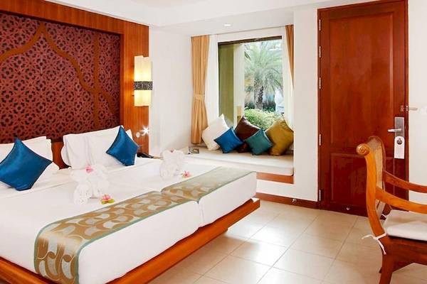 Ein elegantes Hotelzimmer im Rawai Palm Beach Resort mit zwei Betten, blauen Kissen und einem Fenster mit Aussicht auf den Garten.